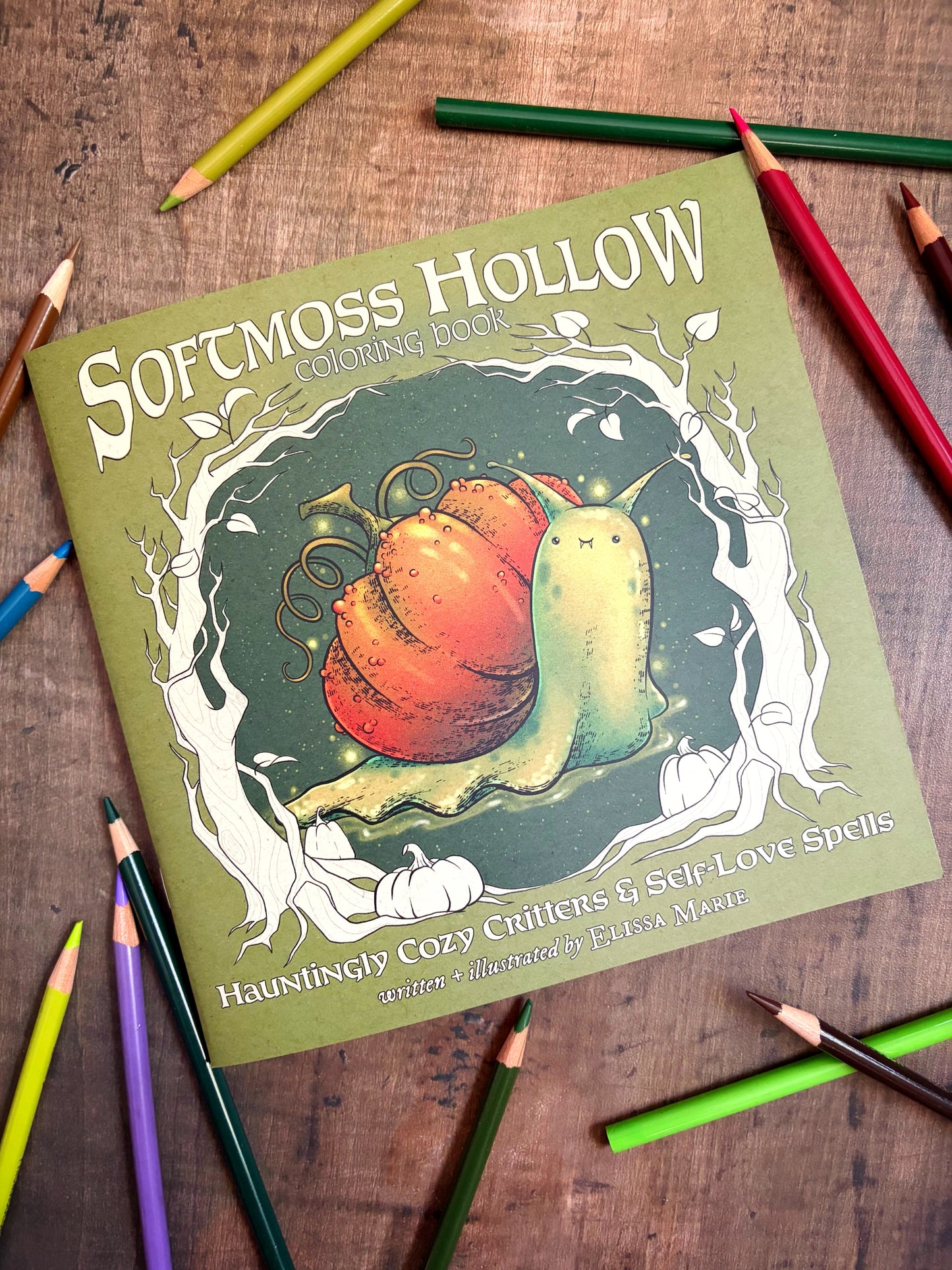 Coloring book front cover titled 'Softmoss Hollow' with a snail illustration on a wooden surface with colored pencils.