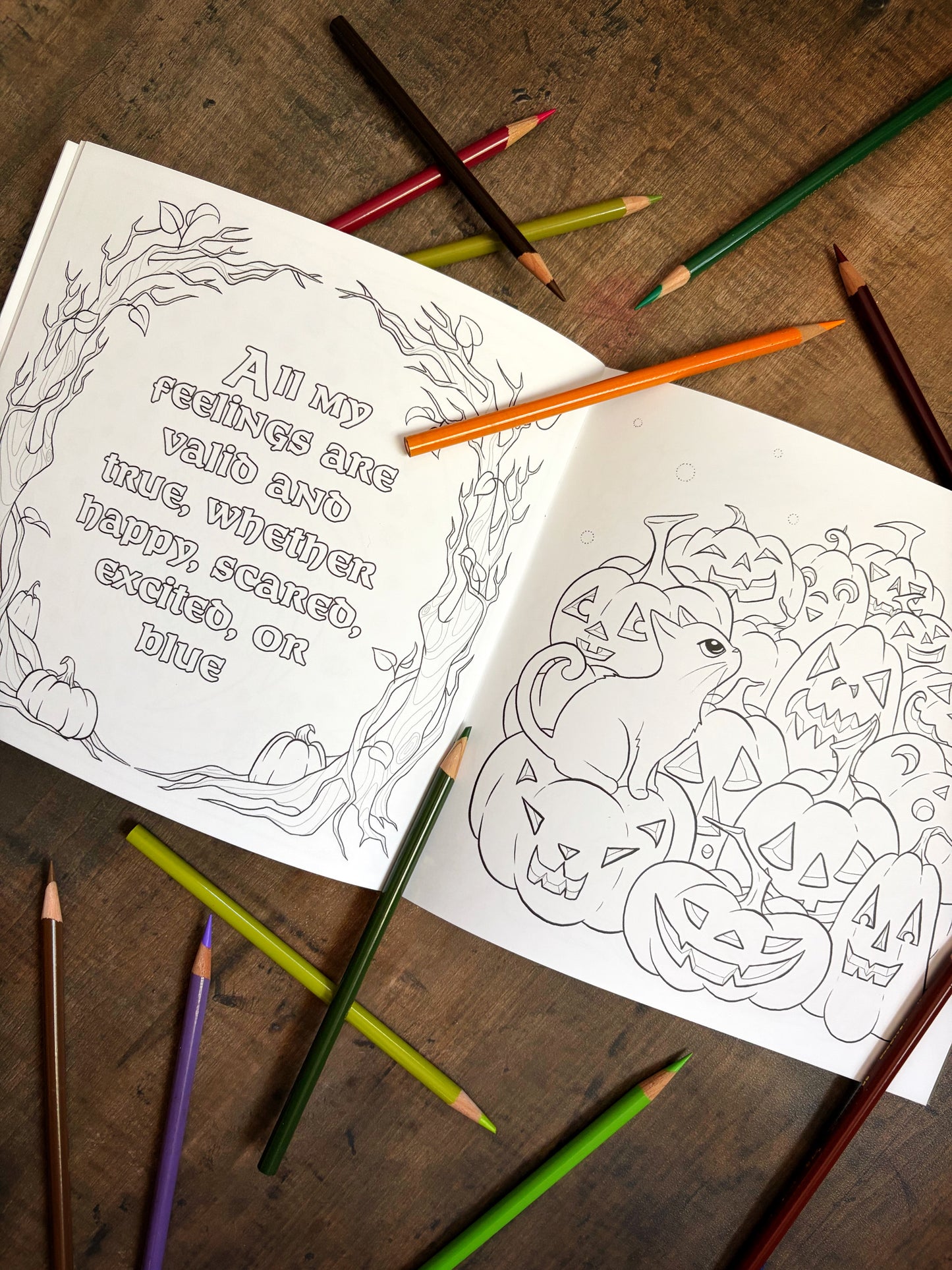 Coloring book with Halloween-themed pages and colored pencils on a wooden surface
