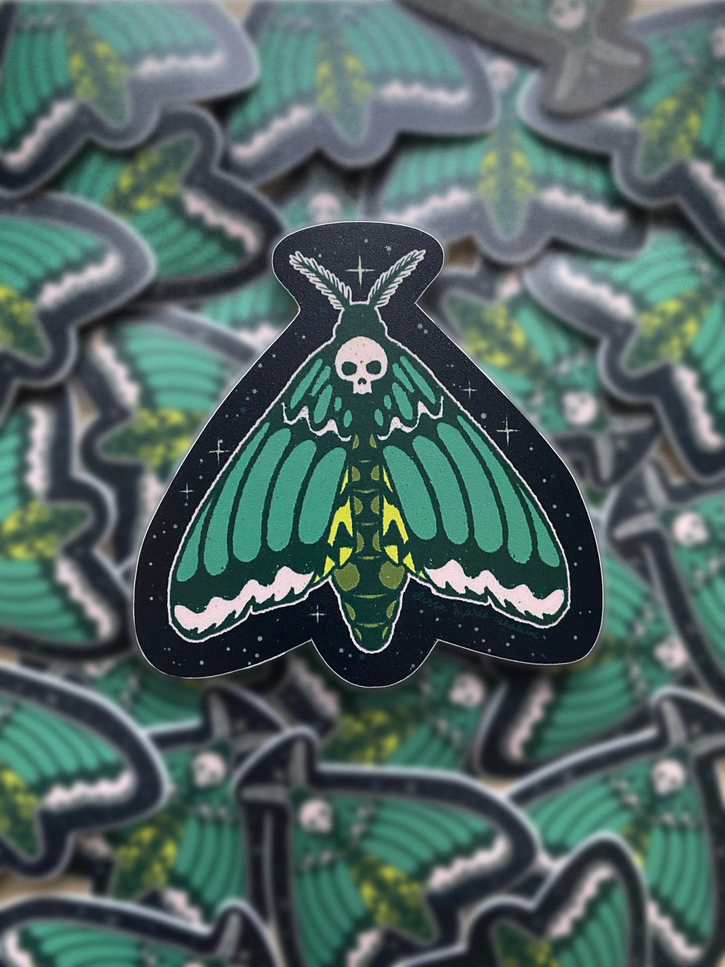 A sticker of a green and black death's head hawk moth with a skull design on its head.