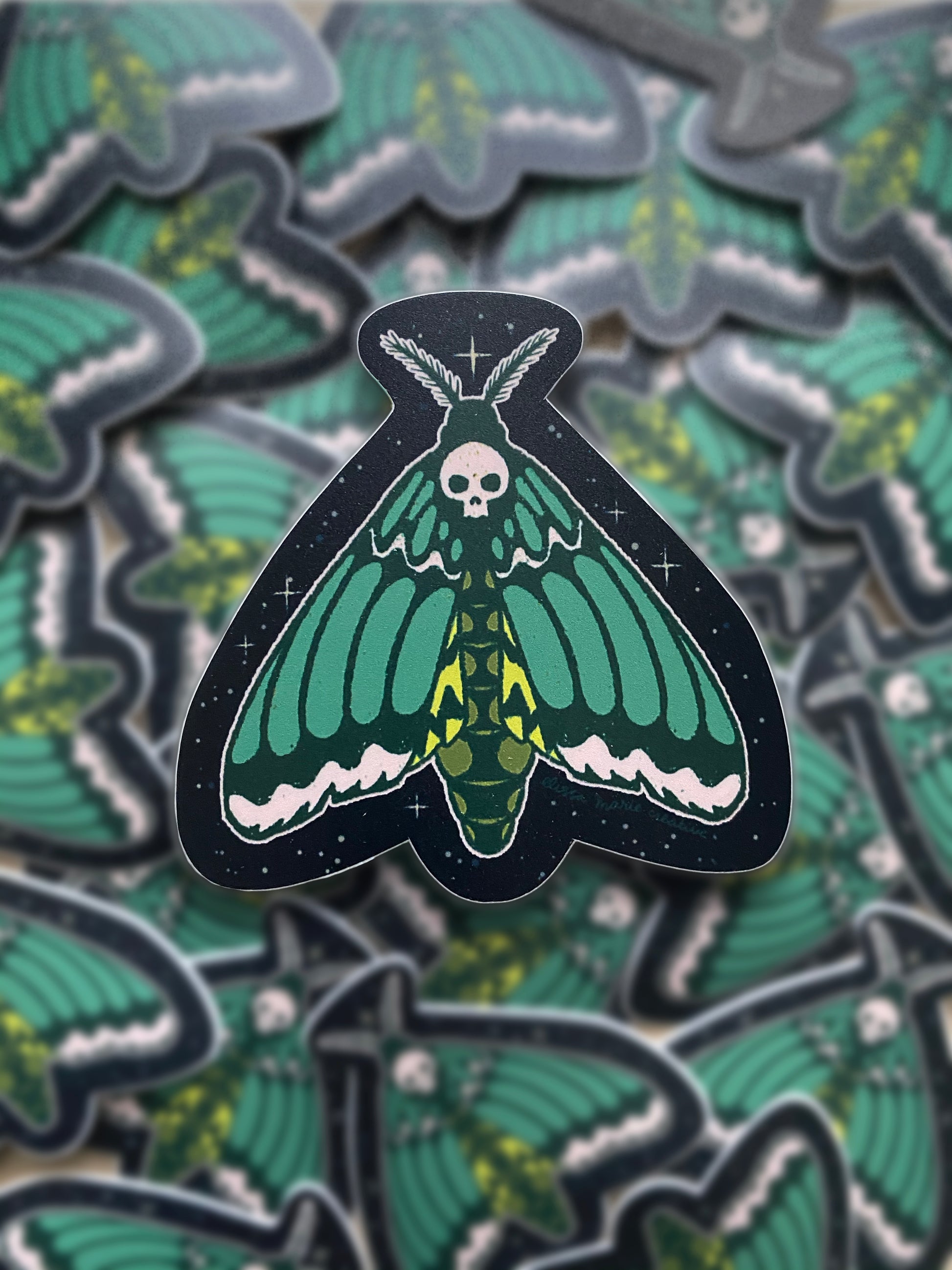 A sticker of a green and black death's head hawk moth with a skull design on its head.