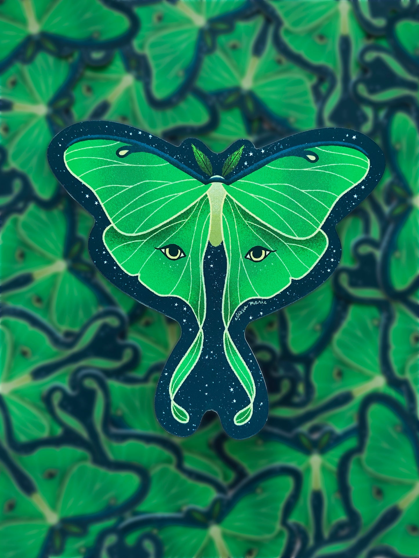 A sticker of a green luna moth with a patterned blue and green background.