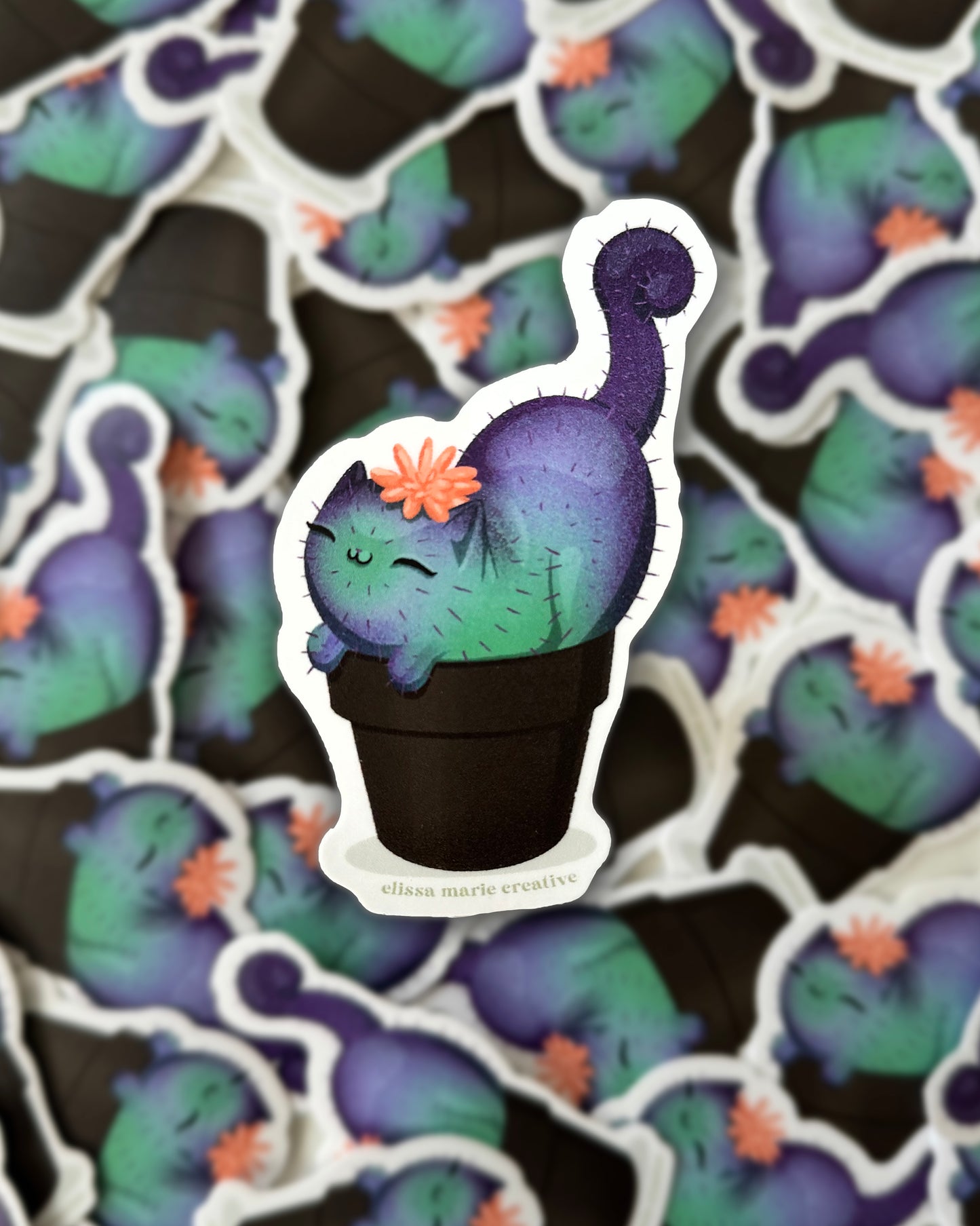 Sticker of a green and purple cactus cat with a peach flower on top, surrounded by repeated patterns of the same sticker.