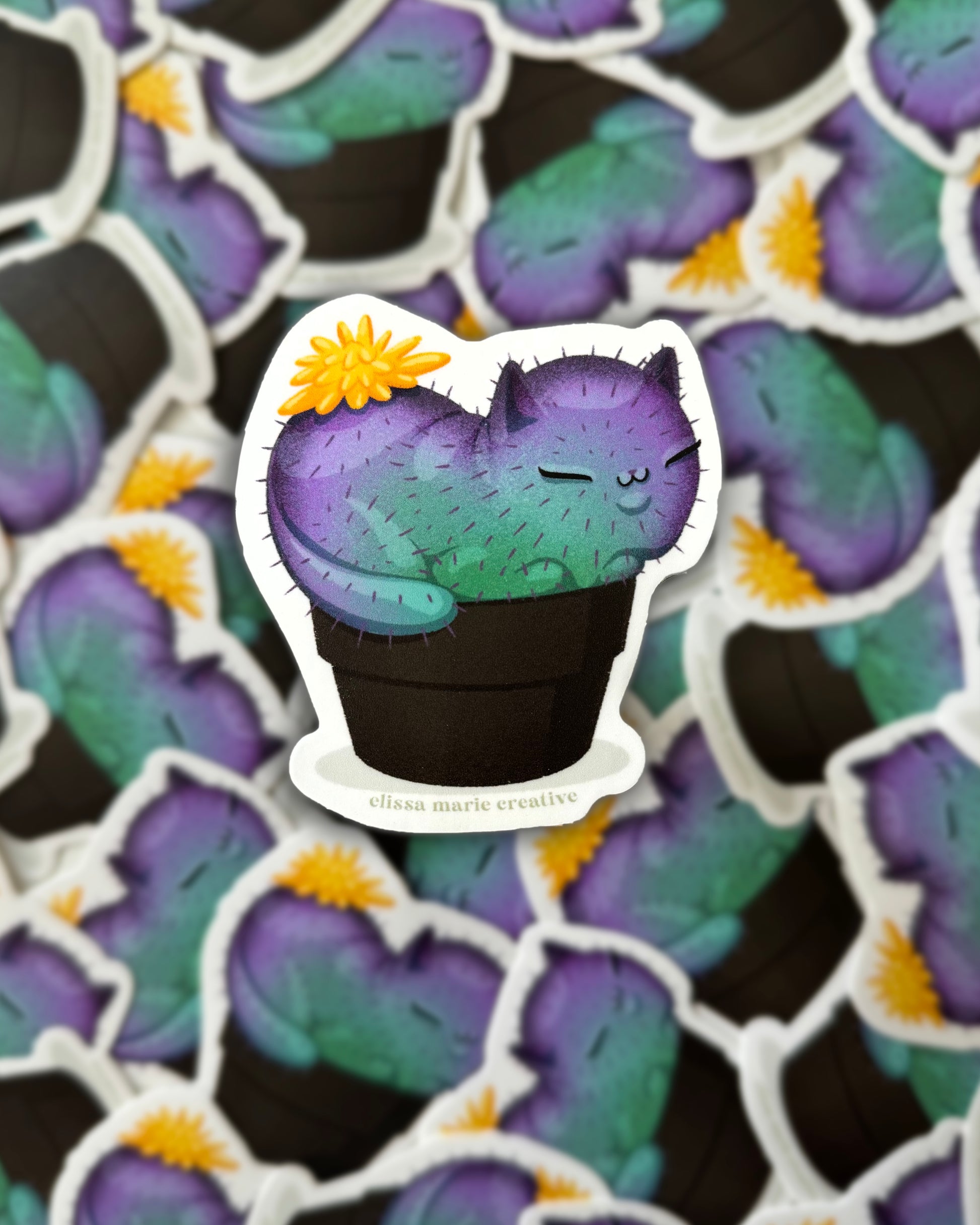 A sticker with a cat-shaped cactus design, featuring a yellow, purple, and black color scheme. The sticker has a matte, die-cut vinyl appearance with a  matte laminated finish.