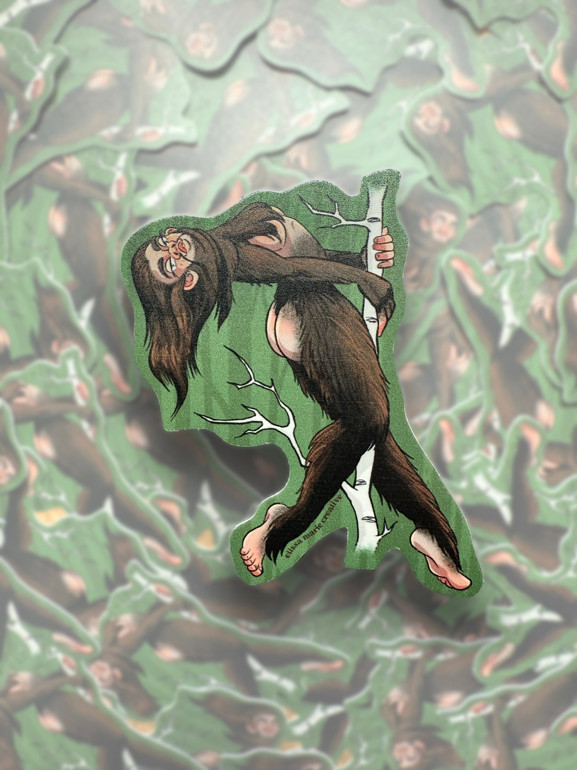 A die-cut sticker with an illustration of a Sasquatch character in a playful pose, designed to be adhered to surfaces.